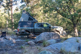 Rugged truck with pop-top camper parked in a rocky forest campsite. A perfect rv rental for your next overland adventure!