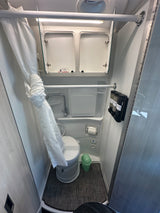 Inside an RV rental: a clean, compact wet bath featuring a toilet, shower with curtain, and mounted soap dispensers.