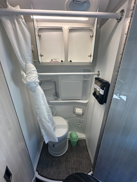 Inside an RV rental: a clean, compact wet bath featuring a toilet, shower with curtain, and mounted soap dispensers.