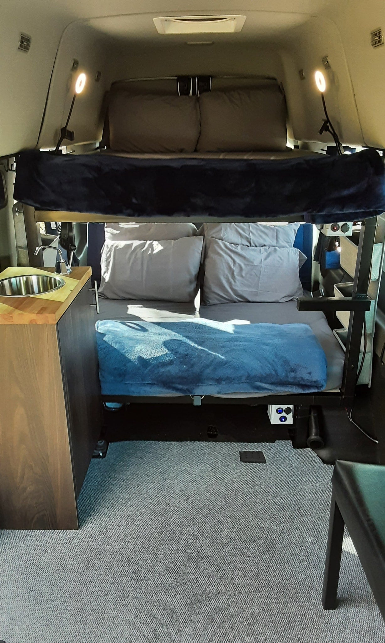  dressed for camping in a vast desert landscape.|This RV rental features comfortable bunk beds and a compact kitchenette with a sink — photo 4