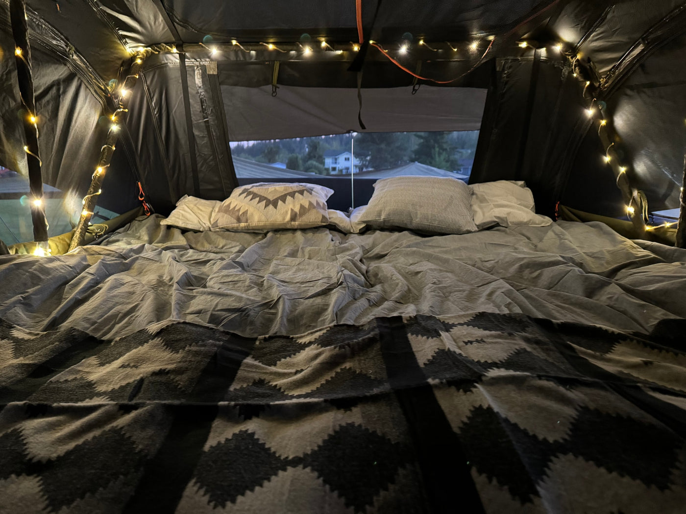Inside a comfy RV rental: bed with pillows, patterned blanket, and string lights. Views outside from the cozy tent. — photo 13