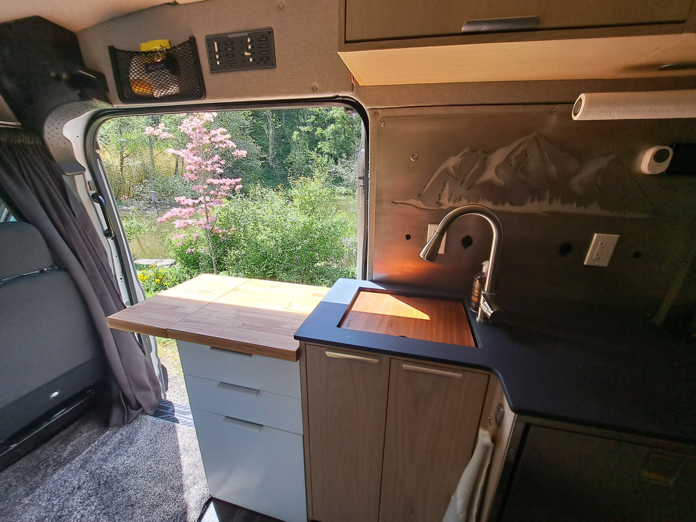 Experience nature with this RV rental! Camper van kitchen featuring a sink, counter, and storage, overlooking a scenic lake and trees. — photo 17