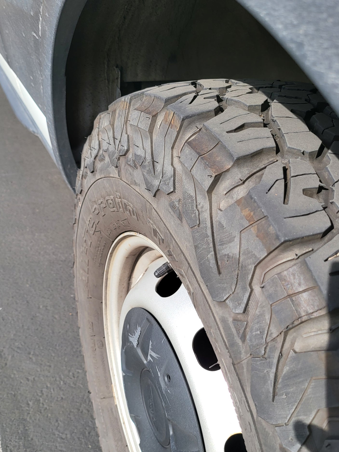 Close-up of an RV rental tire with aggressive tread, on a white wheel with a black center cap, next to the vehicle's fender.