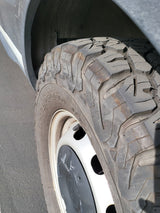 Close-up of an RV rental tire with aggressive tread, on a white wheel with a black center cap, next to the vehicle's fender.