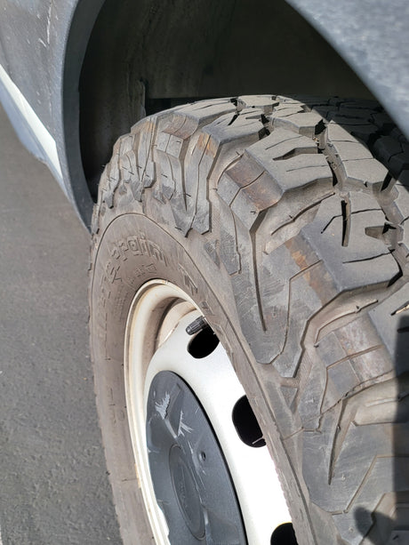 Close-up of an RV rental tire with aggressive tread, on a white wheel with a black center cap, next to the vehicle's fender.