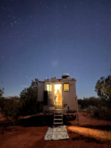 An RV rental illuminated at night, revealing a person inside, set against a stunning, star-filled sky. Perfect for outdoor adventures.