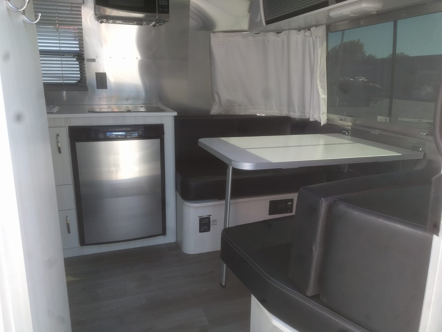 Modern RV rental interior with compact kitchen and dinette, featuring stainless steel appliances and dark seating.