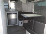 Modern RV rental interior with compact kitchen and dinette, featuring stainless steel appliances and dark seating.
