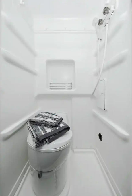 Inside an RV rental: a compact white wet bath featuring a toilet, shower, and folded towel.