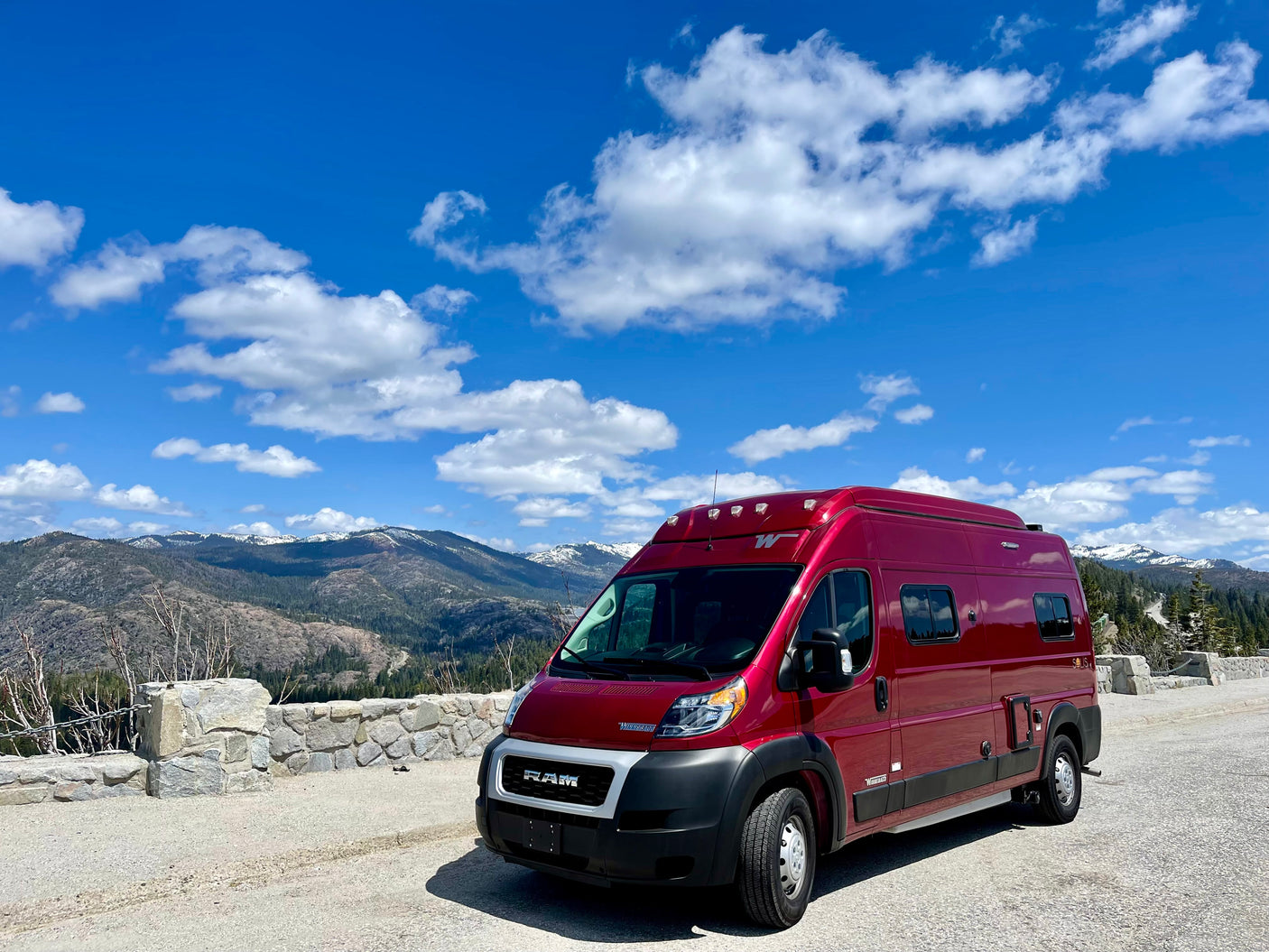 Red Winnebago Solis RV rental parked on a scenic mountain road with snow-capped peaks and a blue sky.