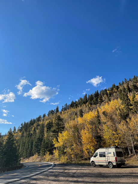 RV rental on a scenic mountain road, nestled among bright yellow autumn aspens and green pines under a blue sky.