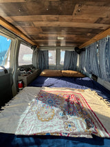 Cozy rv rental van interior with bed, wood ceiling, patterned curtains, fire extinguisher, and fishing rods for adventure.
