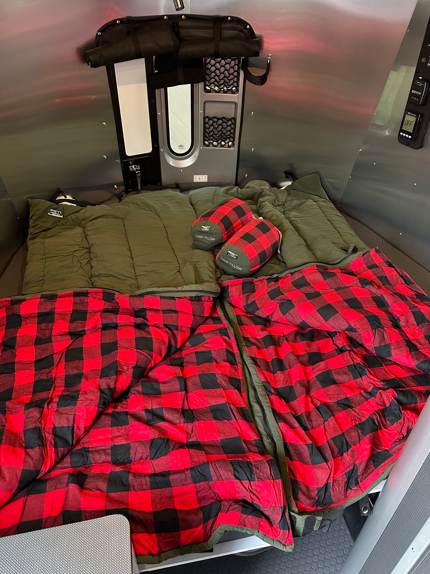 Inside a comfy RV rental: two olive green sleeping bags with red plaid blankets & L.L.Bean pillows. Ready for adventure!
