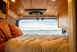 Relax in this cozy RV rental bed with a stunning lake view. Features wooden ceiling, fan, and warm interior lights.