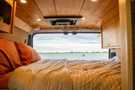 Relax in this cozy RV rental bed with a stunning lake view. Features wooden ceiling, fan, and warm interior lights.
