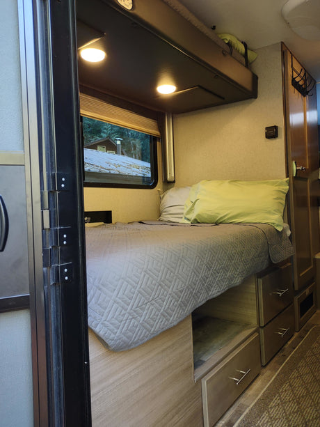 RV rental interior featuring a cozy bed, ample storage, and a scenic window view.