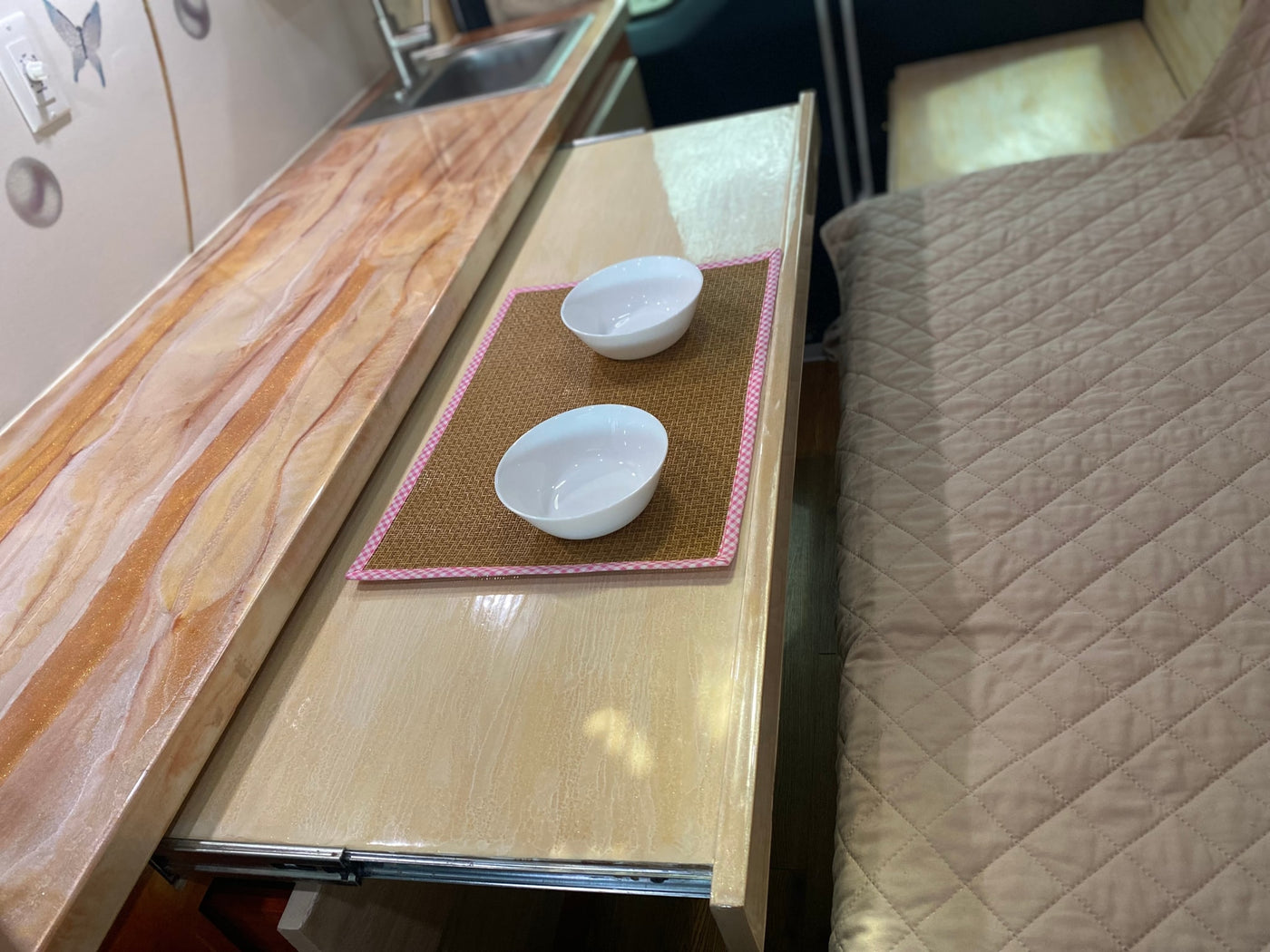 Cozy rv rental interior: kitchen counter, pull-out table with bowls, and quilted bed. — photo 9