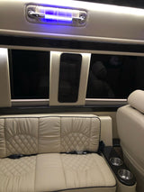 Plush cream leather interior of an RV rental, featuring diamond-stitched seating, cup holders, and overhead blue lighting for comfortable travel.