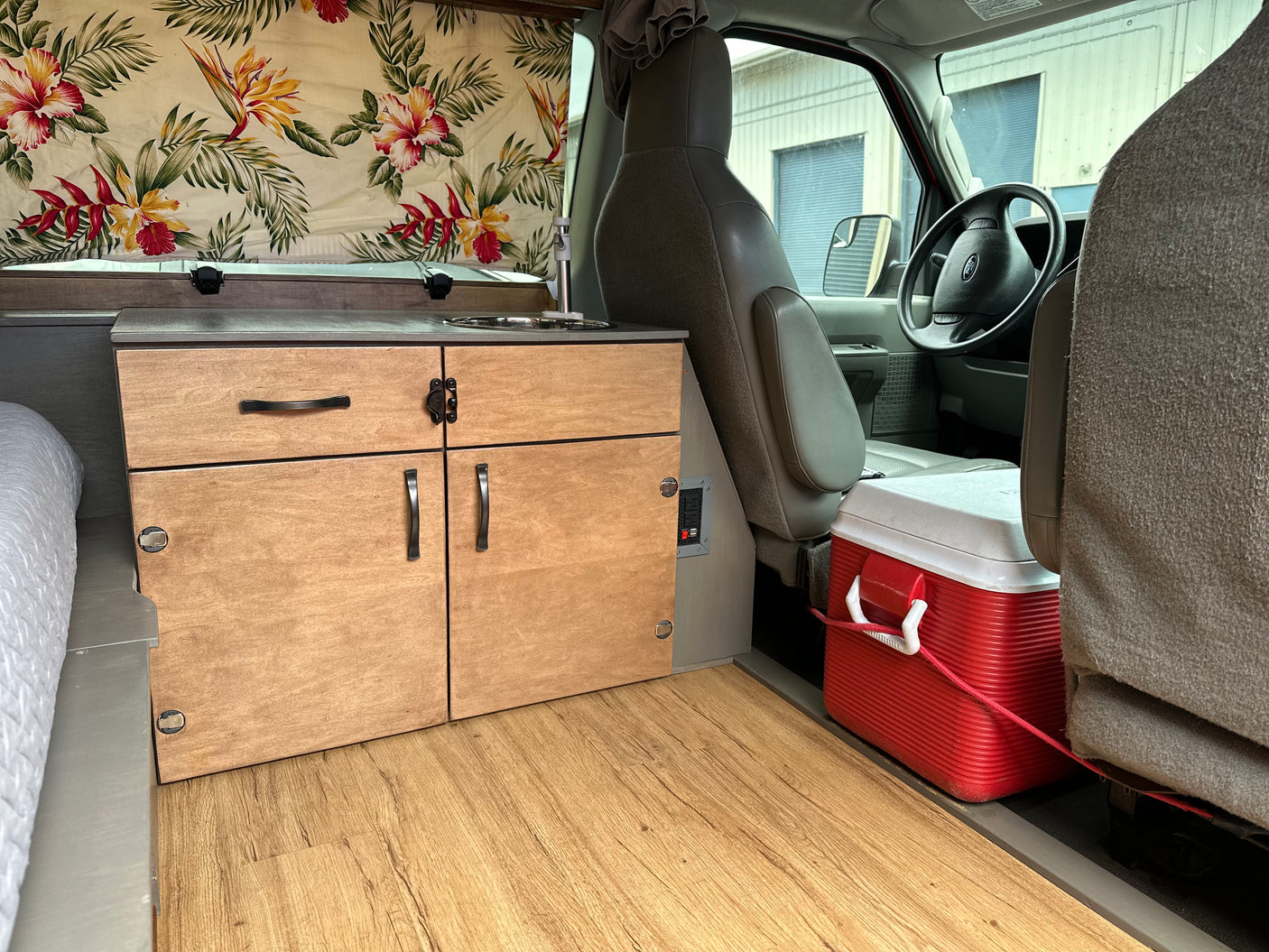 Inside a comfortable RV rental: custom wood cabinetry, sink, bed, and driver's cockpit view. Perfect for travel.