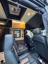 Experience comfort in this well-equipped rv rental interior, featuring a microwave, fridge, fan, and plush seating for your journey.