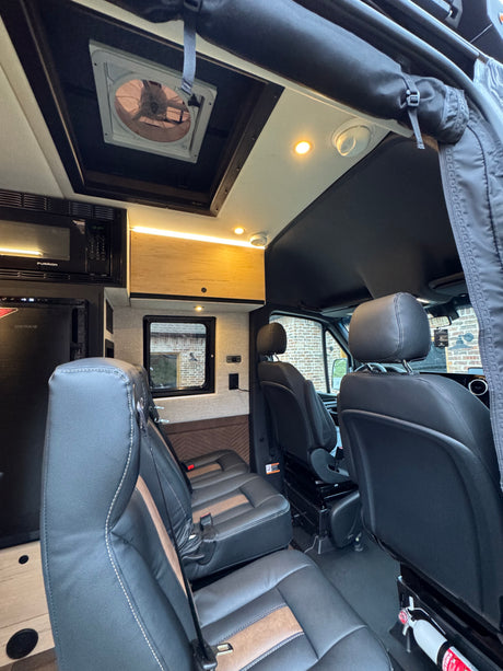 Experience comfort in this well-equipped rv rental interior, featuring a microwave, fridge, fan, and plush seating for your journey.