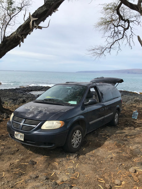 Ocean camping in Hawaii: a dark blue Dodge Caravan (open hatch), a practical RV rental choice.