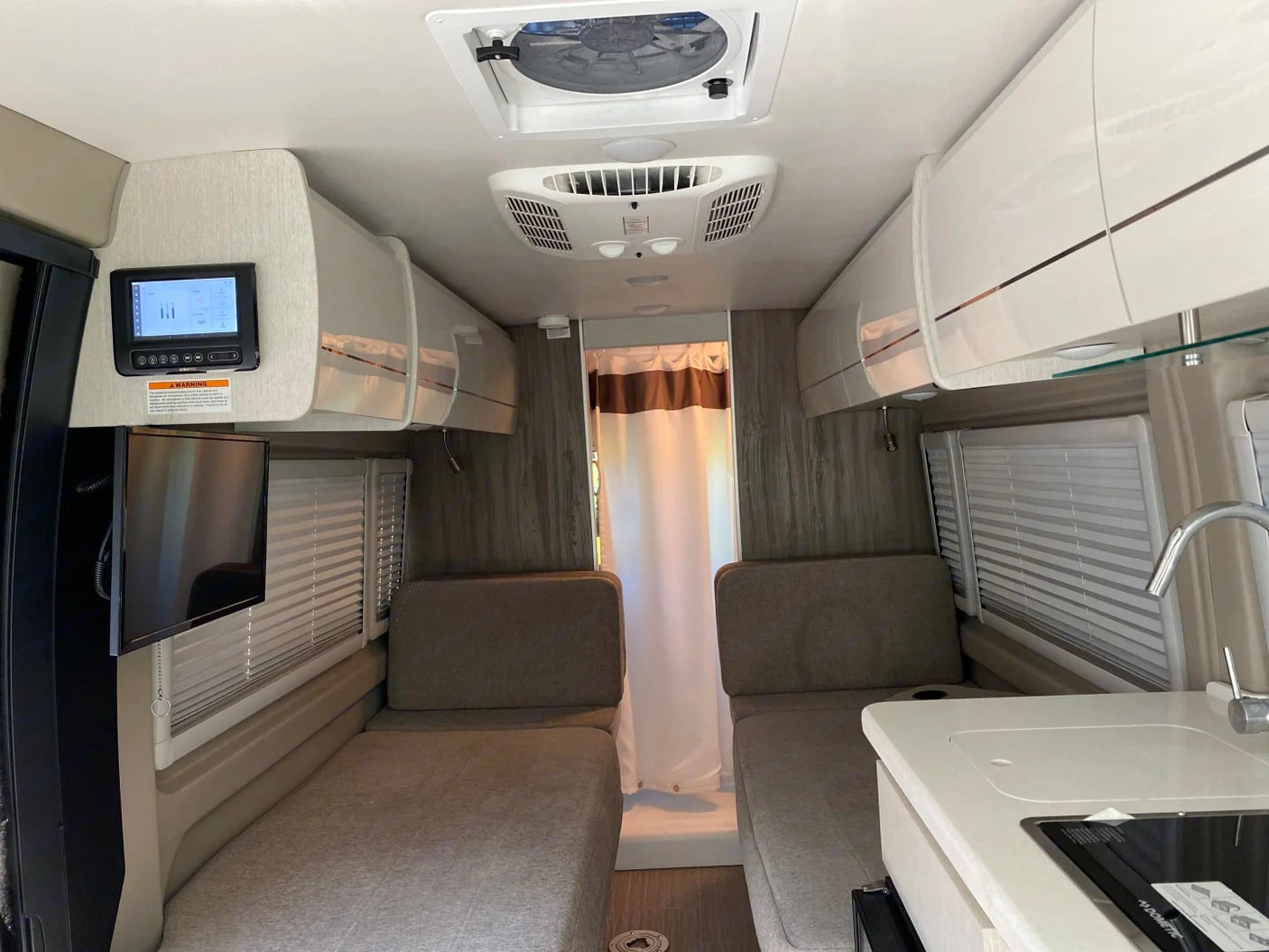 RV rental interior: compact kitchen, twin lounge seats convertible to beds, TV, and overhead storage for comfortable travel.