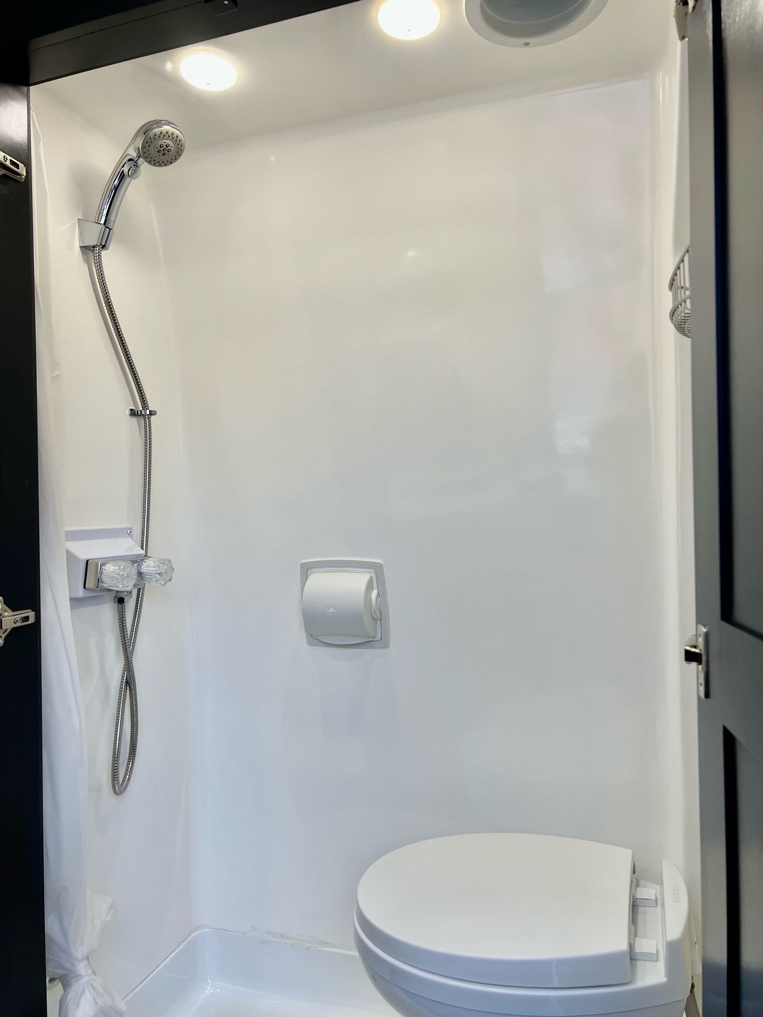 RV rental's compact bathroom features a bright interior with a shower, toilet, and toilet paper dispenser.