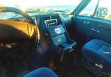 Cozy RV rental interior with ocean view. Dashboard, steering wheel, and blue seats visible, plus a fun shark heart sticker.