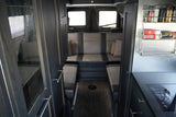 Modern rv rental interior: dark wood cabinets, plush gray seating, and a compact kitchen with a spice rack and stovetop.
