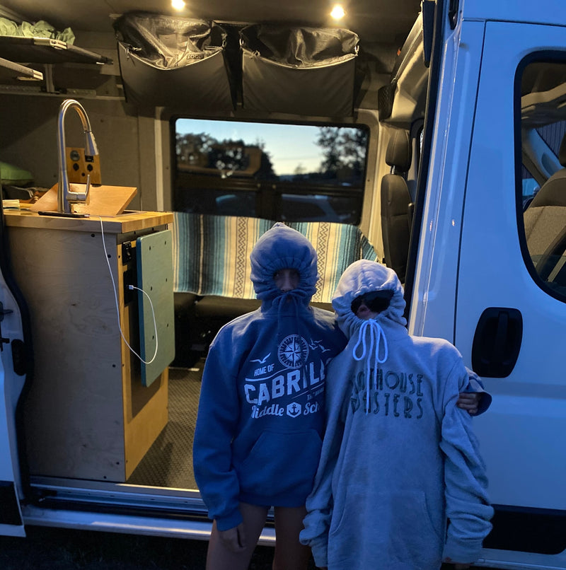 Two people in hoodies stand in an RV rental van, showcasing its cozy interior with a sink, storage, and bench. — photo 5