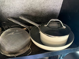 RV rental kitchen gear: beige saucepan with lid, frying pan, and a metal colander, neatly stored.