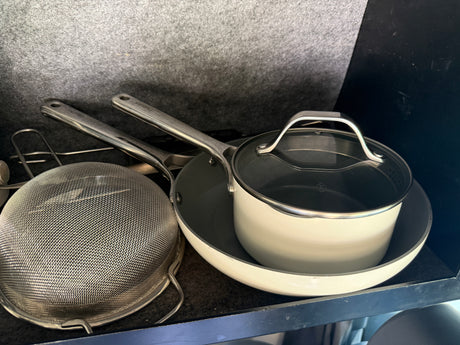 RV rental kitchen gear: beige saucepan with lid, frying pan, and a metal colander, neatly stored.