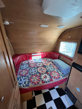 Inviting RV rental interior: a comfy bed with a vibrant quilt, red cushions, and classic checkered flooring.