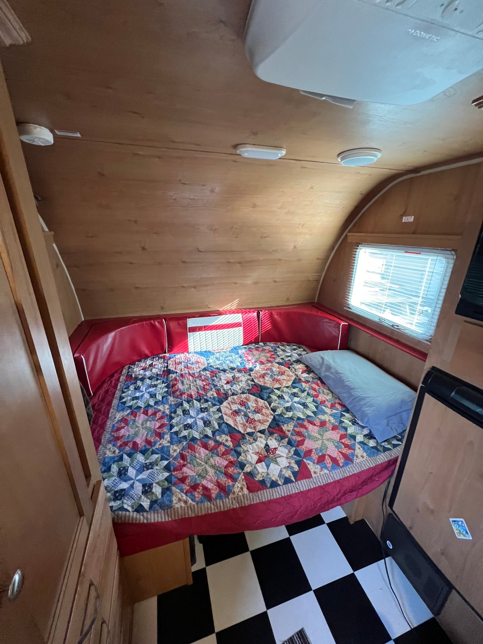 Inviting RV rental interior: a comfy bed with a vibrant quilt, red cushions, and classic checkered flooring.