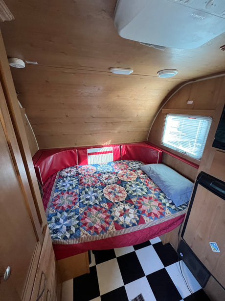 Inviting RV rental interior: a comfy bed with a vibrant quilt, red cushions, and classic checkered flooring.