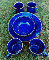 Blue speckled camping plates, bowls, and mugs on grass. Great for an RV rental getaway!