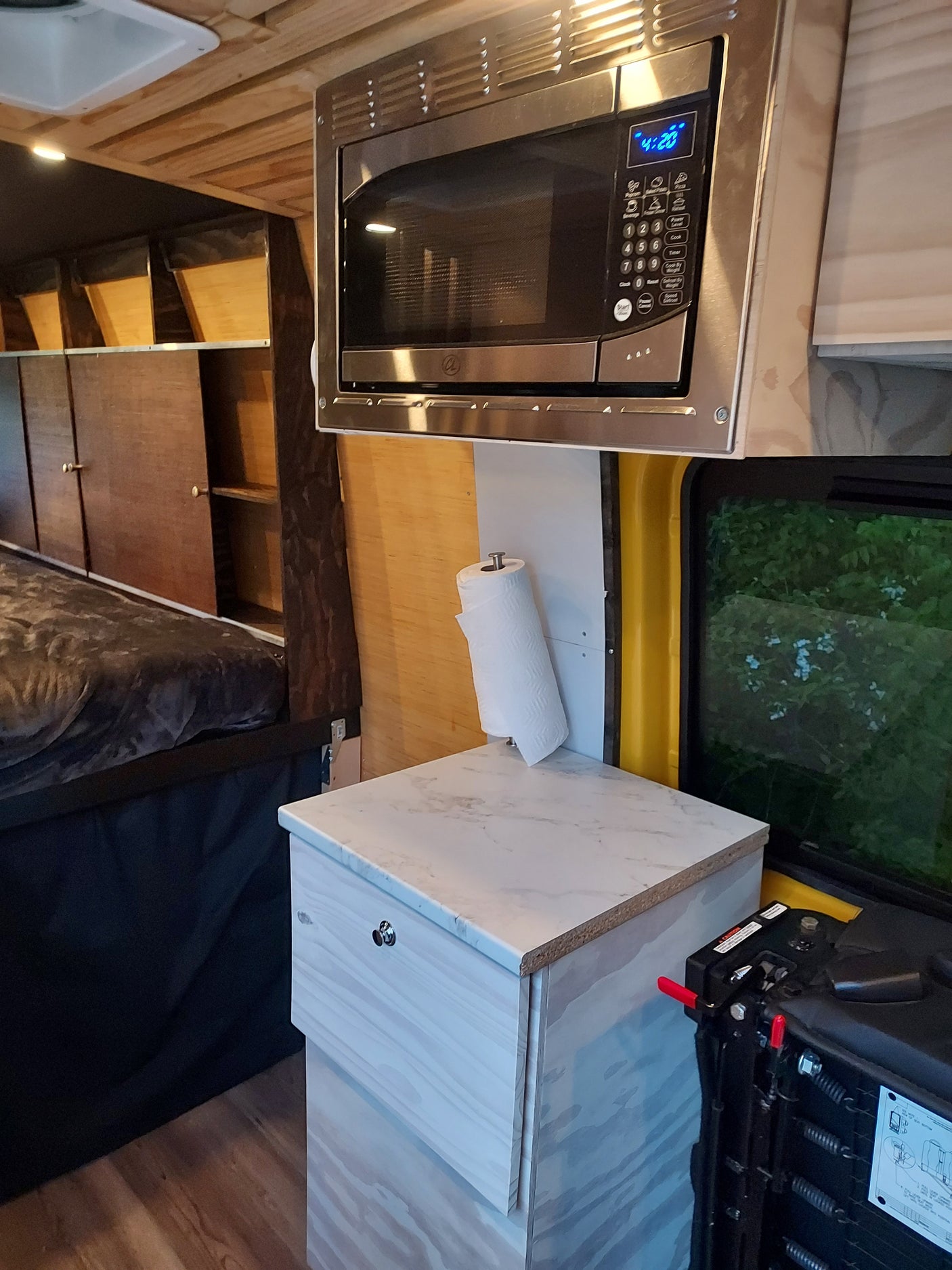 Inside an RV rental: a compact kitchen with microwave, sink, paper towels, and comfortable sleeping area.