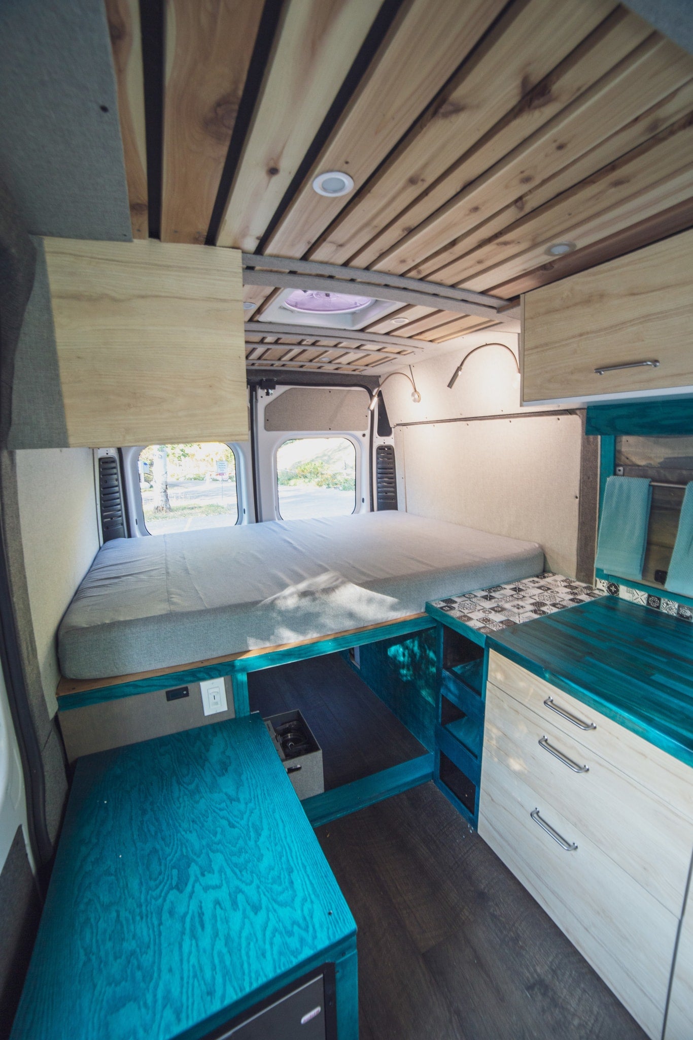 Bright RV rental interior with a comfy bed, unique teal kitchen counter, and slatted wood ceiling. A functional and stylish camper. — photo 6