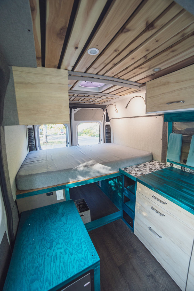 Bright RV rental interior with a comfy bed, unique teal kitchen counter, and slatted wood ceiling. A functional and stylish camper. — photo 6