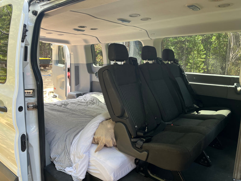 RV rental van interior shows a convertible space with a bed on one side and passenger seats on the other for adaptable travel. — photo 11