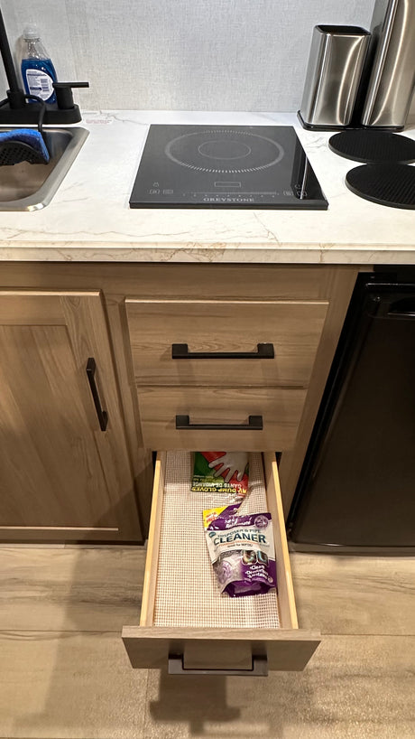 RV rental kitchen showing a compact countertop with sink & induction cooktop. An open drawer reveals RV dump gloves and drain cleaner.