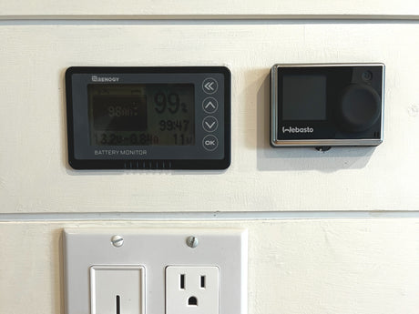 RV rental: Renogy battery monitor (99% charged), Webasto heater control, and an outlet on a white panel wall.