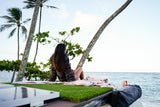 Woman on an RV rental rooftop deck with artificial grass and solar panels, enjoying ocean views from a tropical beach.