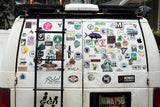 The back of a white RV rental van, adorned with a ladder and countless Hawaii-themed and outdoor adventure stickers.