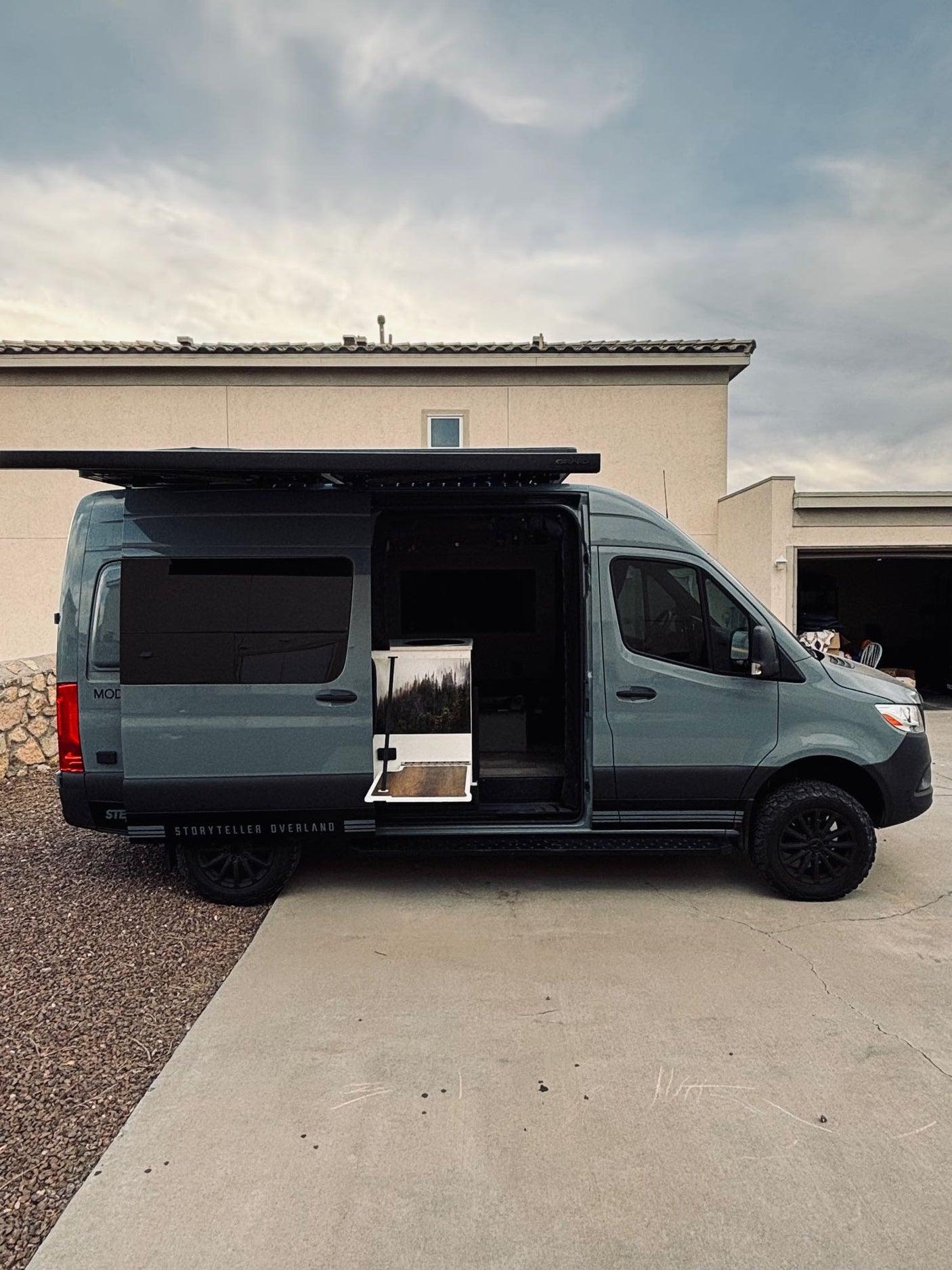 This Storyteller Overland MODE van, perfect for RV rental adventures, has its side door open, revealing a forest design inside.