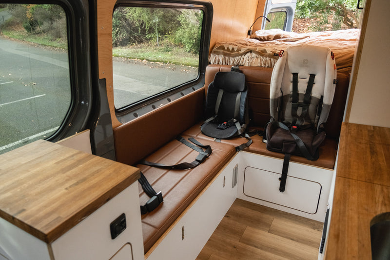 Family-friendly RV rental interior featuring a brown leather bench seat with two child seats, a bed, and wooden accents. — photo 20