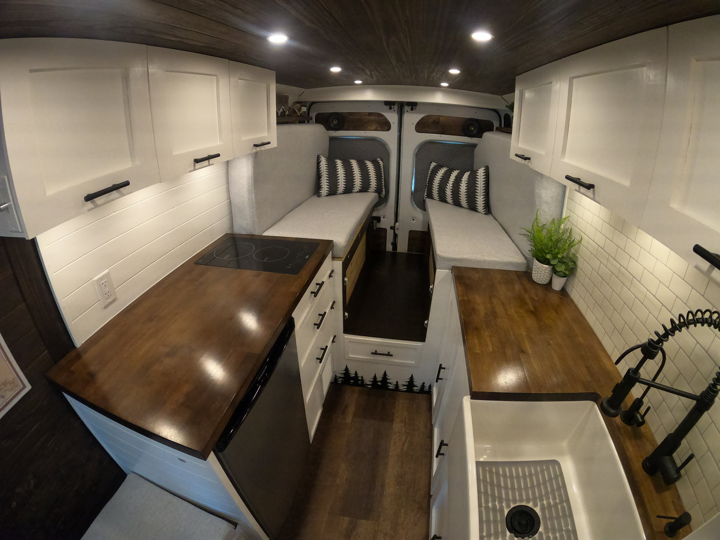 Cozy and functional RV rental interior: wood & white kitchen, dual bench seating/beds, overhead storage, and warm lighting.