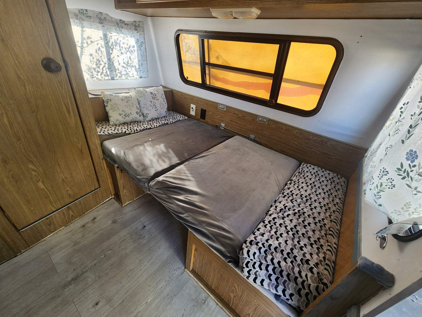 Cozy RV rental interior featuring a bed with patterned cushions, wooden walls, and windows with amber shades.