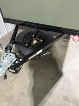 Front section of an RV rental trailer, showcasing the hitch, black chassis, and spare tire mounted underneath on a concrete floor.